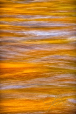 The fall folirage is reflected as an abstract red, yellow, and orange glow on the fast flowing water of the Swift River in Albany, NH.